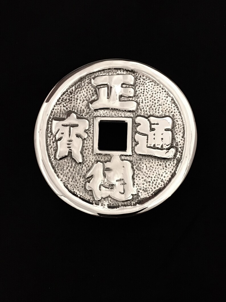 Puede incluir: Una moneda china de plata con un agujero cuadrado en el centro y caracteres chinos alrededor del borde.