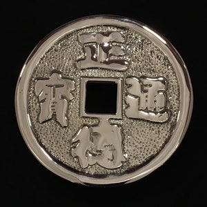 Puede incluir: Una moneda china de plata con letras en relieve y un agujero cuadrado en el centro. La moneda presenta los caracteres chinos "正" (Zheng), "通" (Tong), "寶" (Bao) y "錢" (Qian).