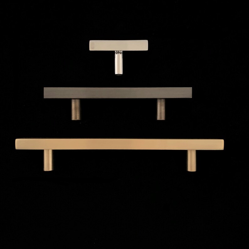 Peut inclure: Trois poign&eacute;es de porte de diff&eacute;rentes tailles et finitions. La poign&eacute;e du haut est une petite poign&eacute;e en T argent&eacute;e. La poign&eacute;e du milieu est une poign&eacute;e rectangulaire plus grande avec une finition nickel bross&eacute;. La poign&eacute;e du bas est la plus grande, une poign&eacute;e rectangulaire avec une finition or bross&eacute;.