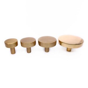 May include: Four gold-toned metal knobs of varying sizes. The knobs are round and have a smooth, brushed finish. They are all mounted on a white background.
