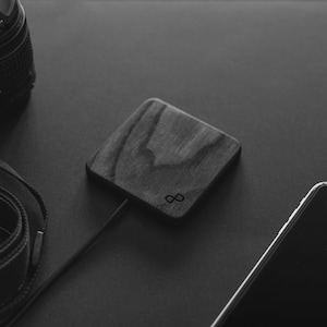 Può includere: Un caricabatterie wireless in legno nero con un logo a forma di infinito. Il caricabatterie è su una superficie nera.