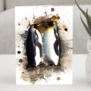 Puede incluir: Dos pingüinos rey con plumas blancas y negras y picos naranjas están de pie uno cerca del otro con sus cabezas tocándose. Los pingüinos están pintados en un estilo acuarela con salpicaduras marrones, naranjas y azules en el fondo.