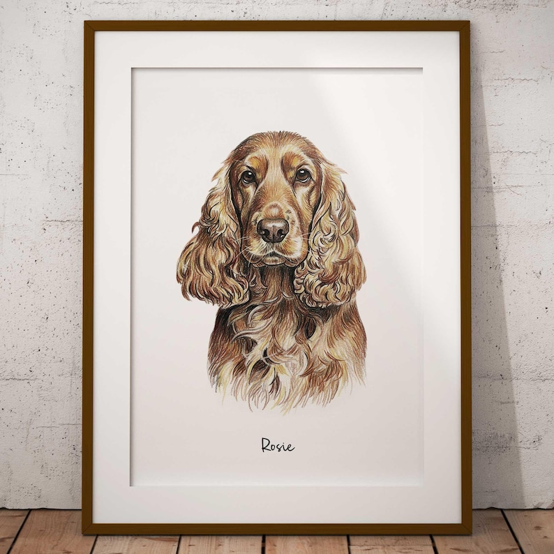 Puede incluir: Retrato enmarcado de un perro Cocker Spaniel con pelaje marr&oacute;n y canela. El nombre del perro, "Rosie", est&aacute; escrito en cursiva en la parte inferior de la impresi&oacute;n. La obra de arte se muestra en un passe-partout blanco y un marco de madera marr&oacute;n.