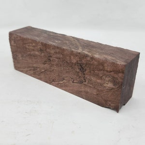 Könnte beinhalten: Ein rechteckiger Block aus dunkelbraunem Holz mit einem einzigartigen Maserungsmuster. Das Holz hat eine natürliche, rustikale Optik.