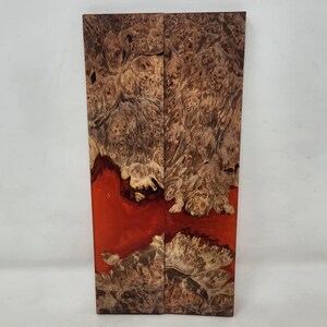 May include: Two wooden slabs with a natural burl pattern and a vibrant red resin inlay. The wood features a mix of light and dark brown tones, creating a unique and textured appearance. The slabs are rectangular and stand vertically.