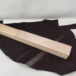 Puede incluir: Una herramienta de afilado de madera con una base de madera marrón claro y una superficie de afilado de cuero marrón claro.