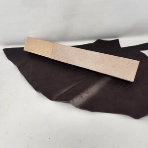 May include: A close-up of a light brown leather swatch on a dark brown leather background. The swatch is textured and has a slightly rough surface.