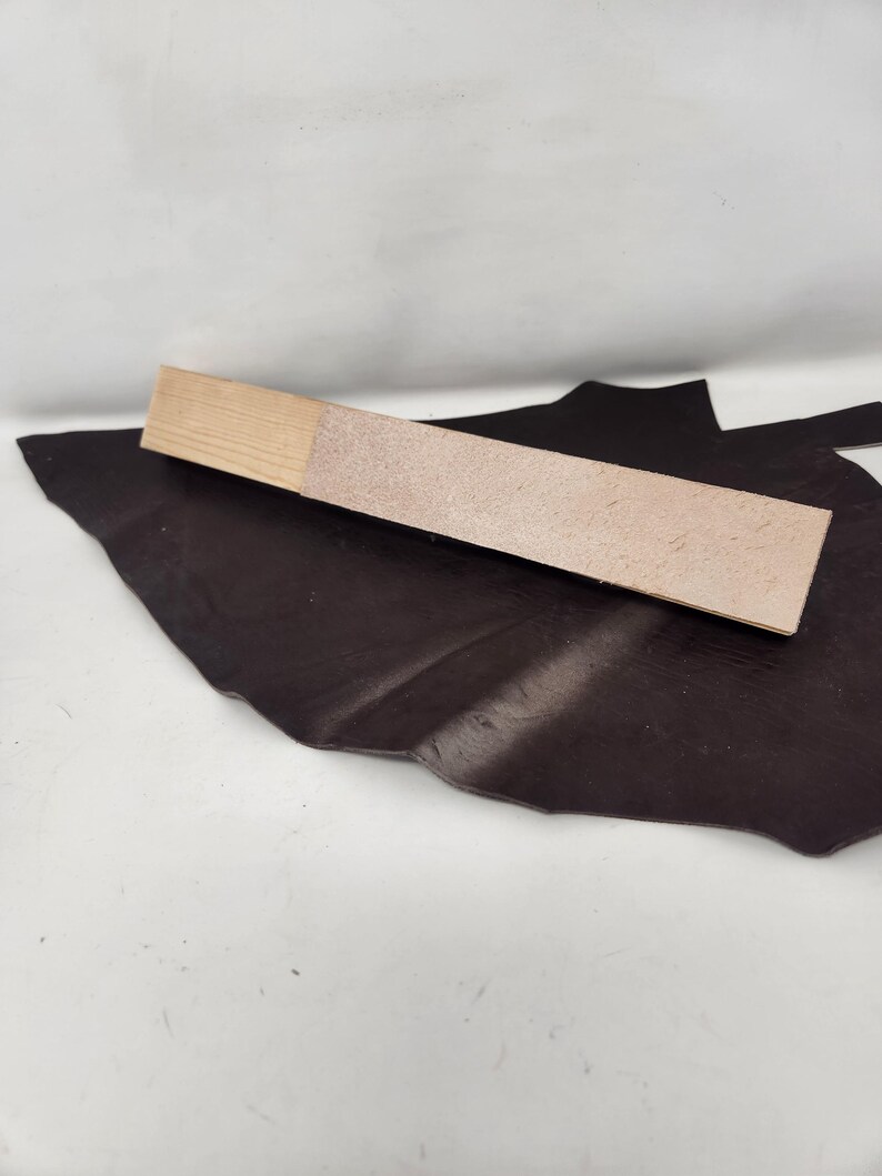 May include: A close-up of a light brown leather swatch on a dark brown leather background. The swatch is textured and has a slightly rough surface.