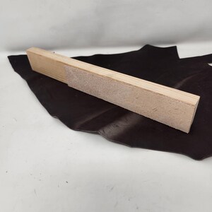 May include: A wooden sanding block with a rough surface. The block is light brown and has a rectangular shape.
