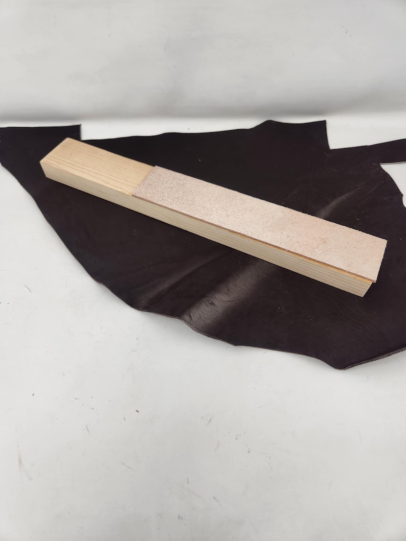 May include: A wooden sharpening tool with a light brown wooden base and a light brown leather sharpening surface.