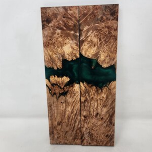 May include: Two wooden slabs with a dark green river of resin running through the center. The wood has a light brown, swirling grain pattern. The resin appears to be a deep, emerald green color.