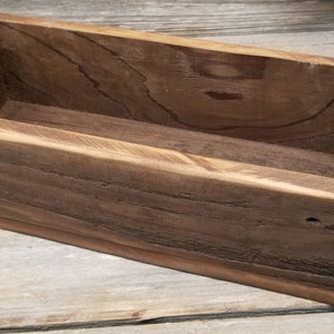 May include: A rectangular wooden box with a dark brown finish. The box is open at the top and appears to be handmade. The wood grain is visible, adding to the rustic aesthetic. The box is likely used for storage or display.
