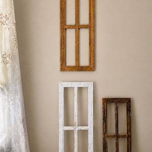 May include: Three rectangular wooden window frames with a vertical and horizontal muntin bar dividing each into four panes. One frame is finished in a warm brown wood tone, one is painted white with a distressed texture, and one is a dark brown.