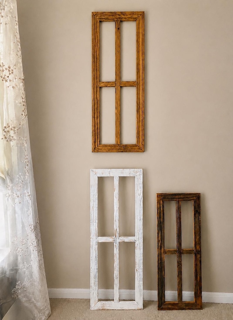 May include: Three rectangular wooden window frames with a vertical and horizontal muntin bar dividing each into four panes. One frame is finished in a warm brown wood tone, one is painted white with a distressed texture, and one is a dark brown.