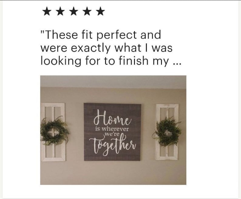 Pode incluir: Uma placa de madeira cinza com letras brancas que diz "Home is wherever we're together". A placa est&aacute; pendurada em uma parede com duas molduras de janelas de madeira branca de cada lado. Cada moldura de janela tem uma coroa verde.