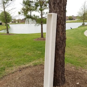May include: A long, white wooden planter box with a rustic finish. The planter is leaning against a tree trunk in a park setting.