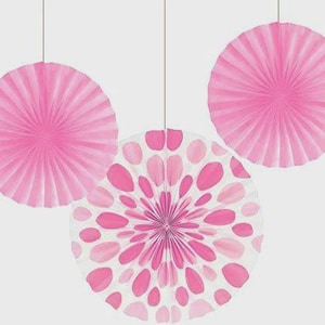 Puede incluir: Tres decoraciones de abanicos de papel rosa colgando de cuerdas. Dos abanicos son de color rosa liso, mientras que el tercero presenta un fondo blanco con lunares rosas y un diseño floral rosa en el centro. Ideal para fiestas y eventos.