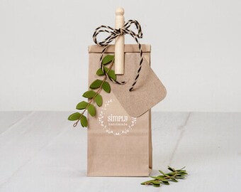 May include: A brown paper gift bag with a wooden stick tied with black and white twine. The bag has a white circle with the text "simply handmade" on it. A small green plant is hanging from the bag.