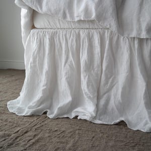 May include: White linen bed skirt with a ruffled edge. The skirt is made of a soft, natural fabric and has a relaxed, casual look.