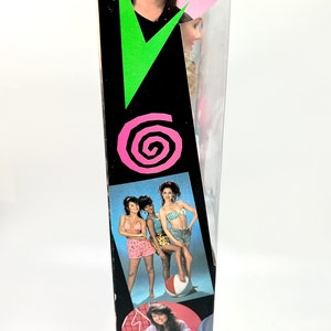 May include: A black and pink box with a picture of a doll on the front. The doll has brown hair and is wearing a black shirt. The box also has a picture of a group of girls in swimsuits. The box says "Model 6-116" and has a barcode.