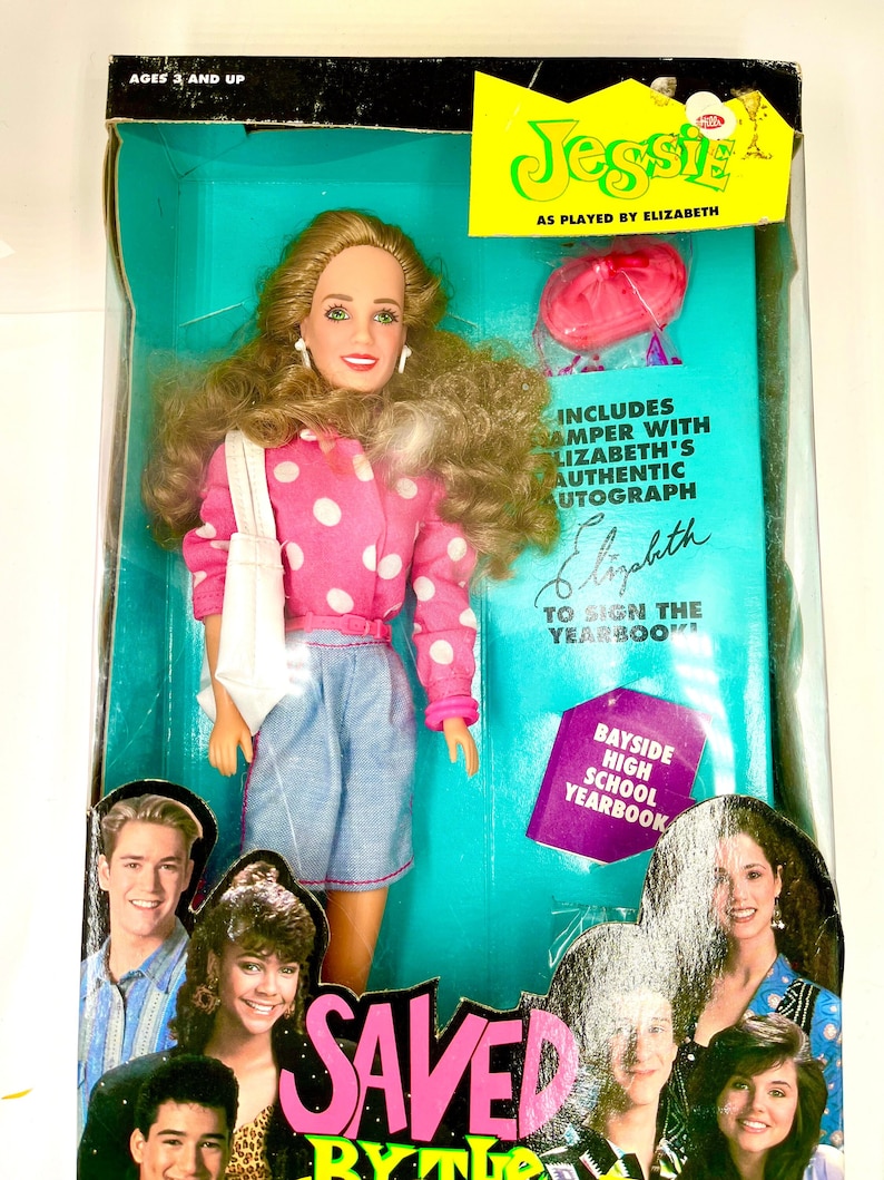 May include: A doll of Jessie Spano from the TV show Saved by the Bell. The doll is wearing a pink polka dot shirt, blue denim shorts, and a white bag. The doll is holding a pink balloon. The box includes a replica of the Bayside High School yearbook with a signature from Elizabeth Berkley, who played Jessie Spano on the show.