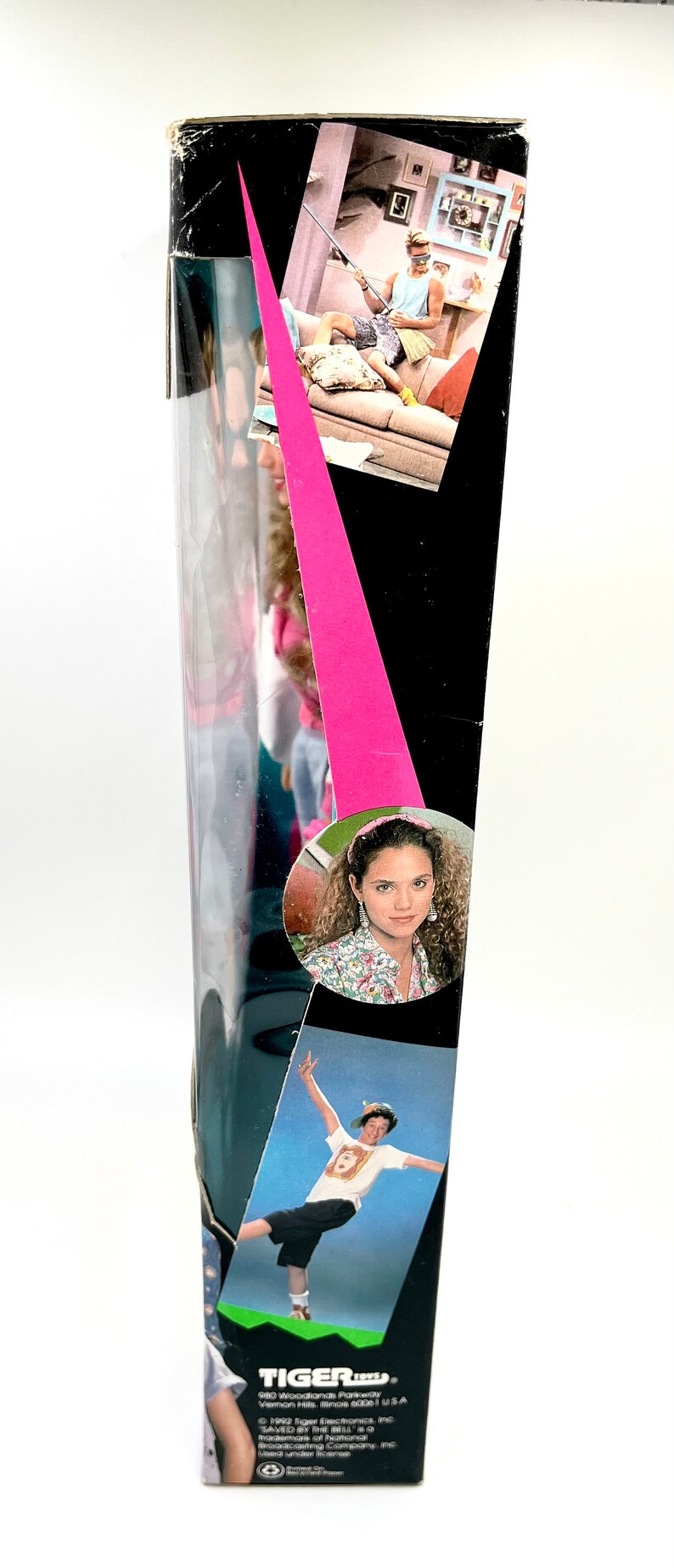 May include: A box for a Tiger Electronics game called "Saved by the Bell". The box is black with a pink stripe and features images of the characters from the show. The text on the box reads "Tiger Electronics, Inc. 980 Woodland Parkway Vernon Hills, Illinois 60061 U.S.A. &copy; 1992 Tiger Electronics, Inc. SAVED BY THE BELL is a trademark of National Broadcasting Company, Inc. Manufactured by Tiger Electronics, Inc. All rights reserved."