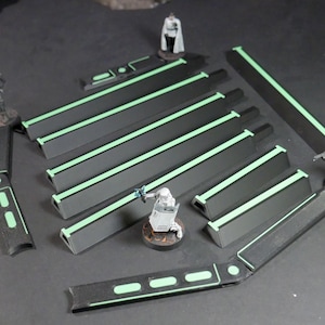 May include: A set of dark gray miniature terrain pieces featuring bright green glowing-style accents, including several long rectangular barriers and two curved corner sections, accompanied by four small painted soldier figurines.