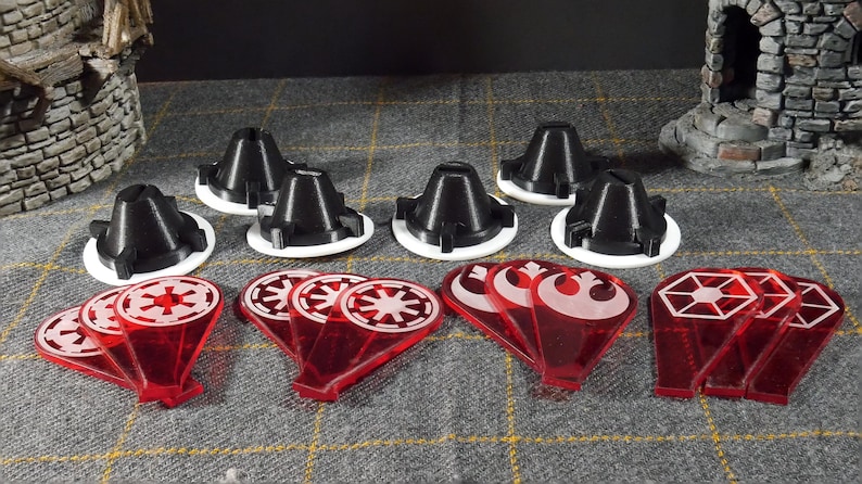 May include: A selection of black and white game pieces, alongside red translucent tokens with white symbols. The items are displayed on a grey patterned surface, possibly for a tabletop game or hobby.