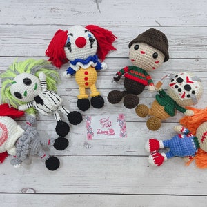 Puede incluir: Una colección de muñecos de ganchillo hechos a mano que representan personajes de películas de terror, incluyendo un payaso, Beetlejuice, Freddy Krueger, Jason Voorhees y Chucky. Cada muñeco presenta colores y detalles distintivos, con un aspecto artesanal.