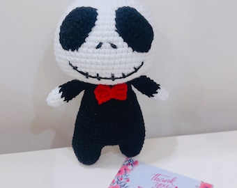 Peut inclure: Poupée au crochet faite à la main, ressemblant à un personnage avec une tête blanche, des yeux noirs et un sourire cousu. La poupée porte un costume noir avec un nœud papillon rouge. Une petite carte avec le texte "Thank you ZInny" est au premier plan.
