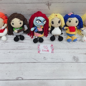 Puede incluir: Seis muñecas de ganchillo hechas a mano con varios colores de pelo y atuendos. Las muñecas incluyen personajes con pelo rojo, marrón, azul y amarillo. Cada muñeca tiene un atuendo único, con detalles como un corazón rojo, una camisa verde y un vestido blanco y negro.