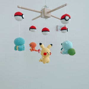 May include: A wooden mobile with crocheted Pokemon characters, including Pikachu, Squirtle, and Charmander. The mobile also features four red and white Pokeballs.