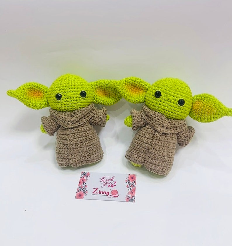 May include: Two crocheted green and brown plush toys with large ears and black eyes. The toys are sitting on a white surface with a small card that says "Thank you! Z.Inky".