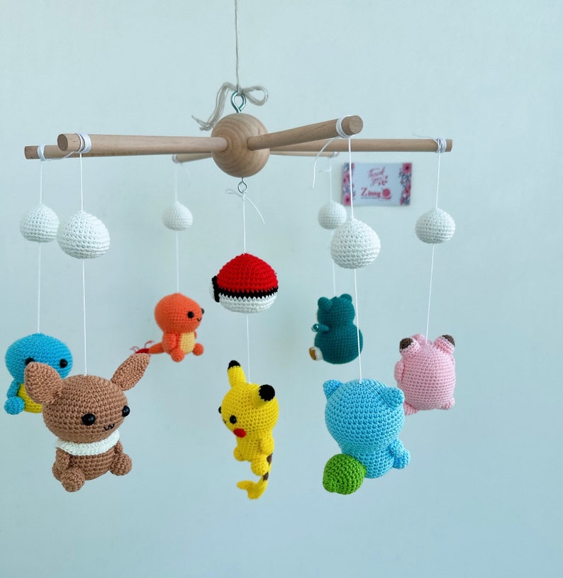 May include: A wooden baby mobile with crocheted Pokemon characters, including Pikachu, Bulbasaur, Charmander, Squirtle, and a Pokeball. The mobile also features white crocheted clouds.