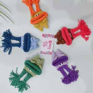 May include: Five crocheted plush toys with different colored hats and faces. The toys are all wearing hats with long crocheted braids. The hats are orange, brown, green, purple, and blue.