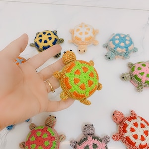May include: A collection of eight crocheted turtle toys in various colors, including green, orange, pink, blue, and yellow. Each turtle has a detailed shell pattern and black eyes.