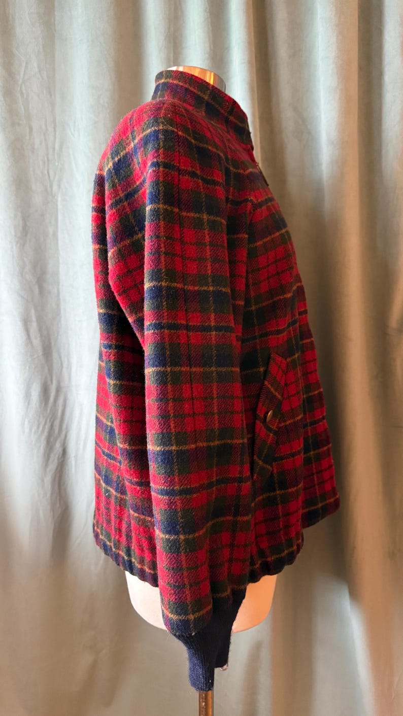 Puede incluir: Chaqueta a cuadros rojos, verdes, azules y dorados con cuello alzado. La chaqueta tiene cremallera frontal y dos bolsillos. Los pu&ntilde;os y el bajo son de punto azul oscuro.