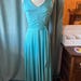 May include: A sleeveless floor-length dress in a solid bright turquoise color. The dress features a V-neckline, a fitted bodice with vertical seams, and a waistline accented by a matching fabric tie belt. The skirt is full and flows downward.