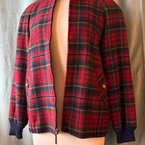 Puede incluir: Chaqueta a cuadros rojos, verdes y azul marino con cremallera y cuello alzado. La chaqueta tiene pu&ntilde;os de canal&eacute; azul marino y botones dorados. La chaqueta se exhibe en un maniqu&iacute;.