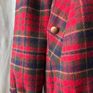 Puede incluir: Primer plano de una chaqueta a cuadros roja, azul y verde. La chaqueta tiene un bot&oacute;n de madera y un pu&ntilde;o azul marino acanalado. La tela tiene un aspecto texturizado. La chaqueta es de estilo cl&aacute;sico.