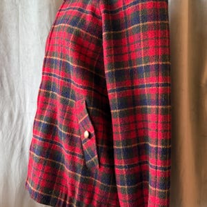 Puede incluir: Chaqueta vintage a cuadros rojos, verdes y azul marino, con cuello alto y botones dorados. La chaqueta tiene un bolsillo con un bot&oacute;n dorado y pu&ntilde;os azul marino. La chaqueta se exhibe en un maniqu&iacute;.