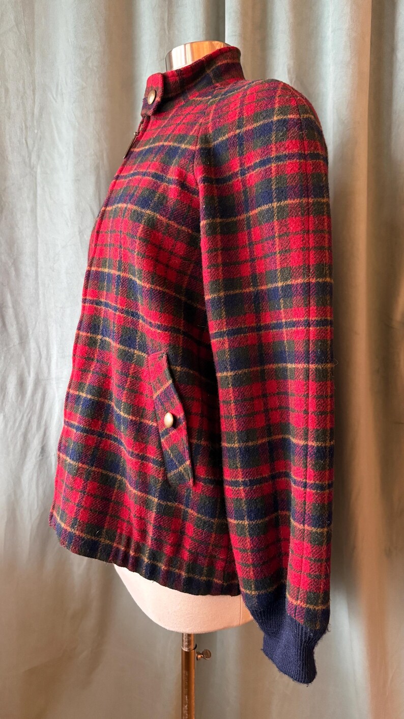 Puede incluir: Chaqueta vintage a cuadros rojos, verdes y azul marino, con cuello alto y botones dorados. La chaqueta tiene un bolsillo con un bot&oacute;n dorado y pu&ntilde;os azul marino. La chaqueta se exhibe en un maniqu&iacute;.