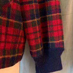 Puede incluir: Primer plano de un patr&oacute;n de cuadros rojos, azul marino y verde en una prenda. El pu&ntilde;o de la manga es azul marino. El dise&ntilde;o de cuadros presenta un patr&oacute;n repetitivo de cuadrados y l&iacute;neas.