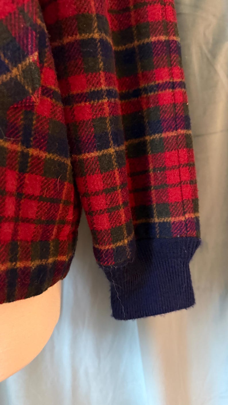 Puede incluir: Primer plano de un patr&oacute;n de cuadros rojos, azul marino y verde en una prenda. El pu&ntilde;o de la manga es azul marino. El dise&ntilde;o de cuadros presenta un patr&oacute;n repetitivo de cuadrados y l&iacute;neas.