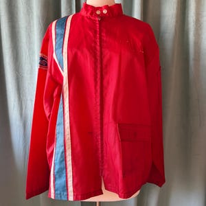 May include: A bright red jacket with a high collar and a vertical stripe design on the left side. The stripe features a light blue and white colour scheme. The jacket has a pocket on the right side and is buttoned up the front.
