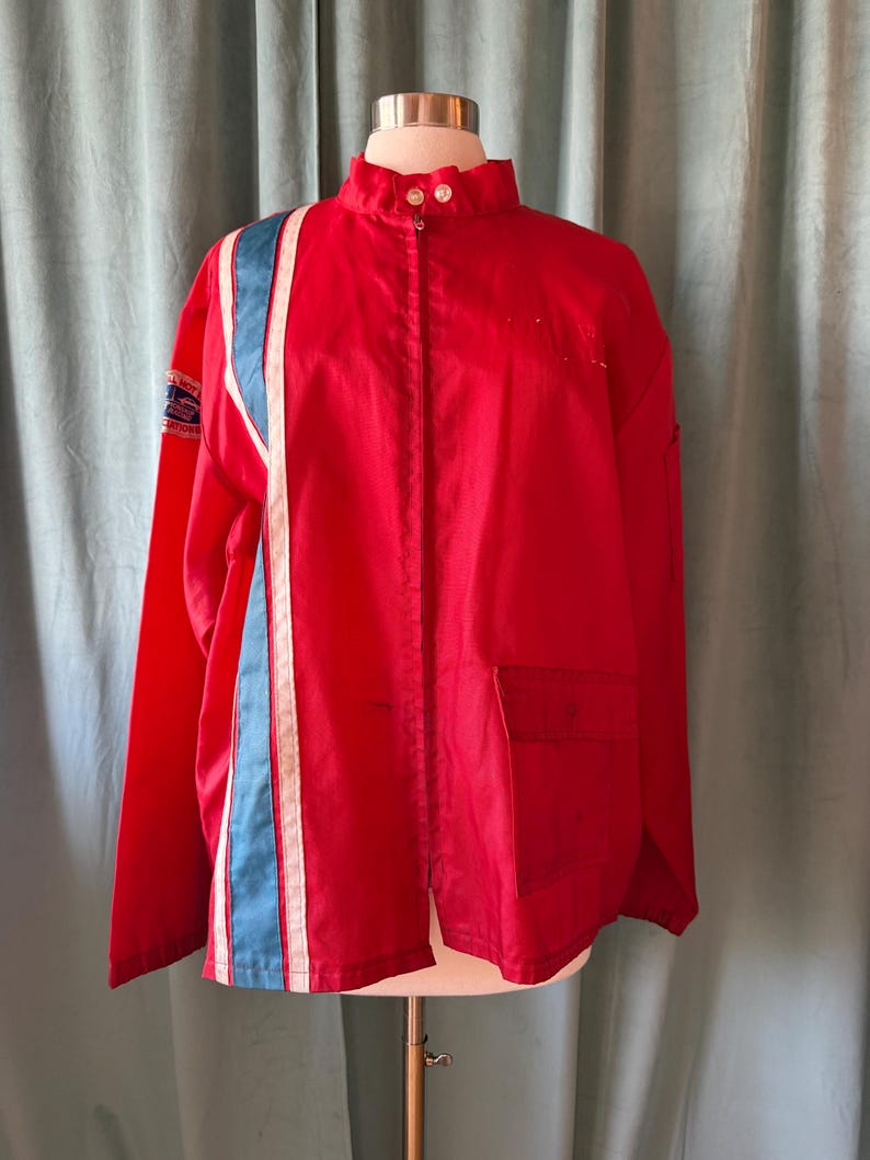 May include: A bright red jacket with a high collar and a vertical stripe design on the left side. The stripe features a light blue and white colour scheme. The jacket has a pocket on the right side and is buttoned up the front.