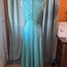 May include: A sleeveless, floor-length turquoise dress displayed on a mannequin. The dress features a high neckline, a fitted bodice with a wide waistband, and a flared skirt. A vertical zipper closure runs down the center of the back of the bodice.