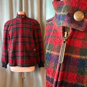 May include: A red, green, and navy plaid jacket with a stand-up collar and a zipper closure. The jacket has two front pockets and navy blue ribbed cuffs. The zipper pull has the word "Pendleton" on it.