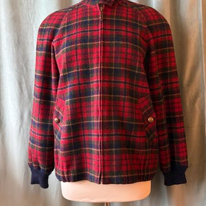 Puede incluir: Una chaqueta a cuadros rojos, verdes y azul marino con cuello alto y cremallera completa. La chaqueta tiene dos bolsillos delanteros con botones y pu&ntilde;os de canal&eacute; azul marino. La chaqueta se exhibe en un maniqu&iacute;.