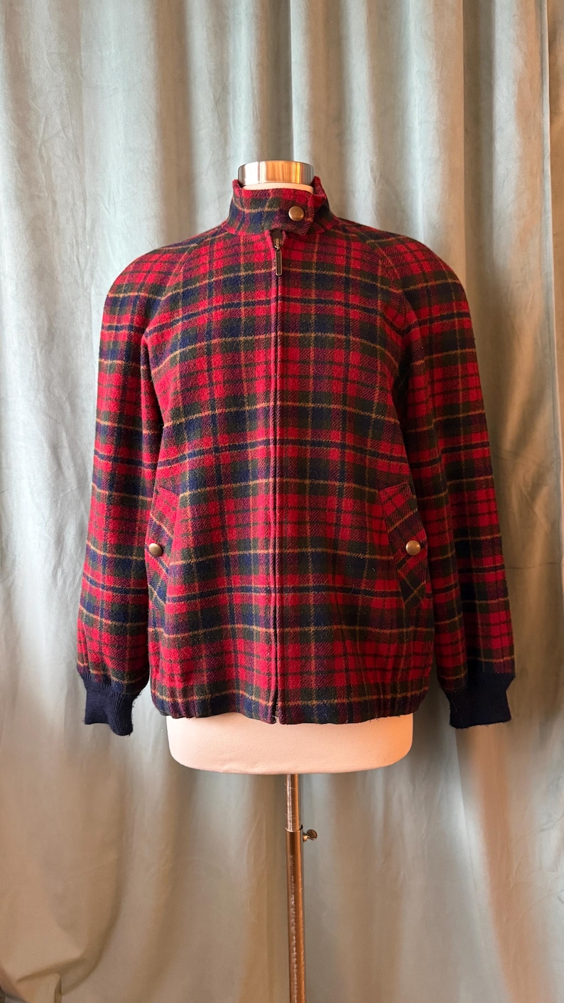 Puede incluir: Una chaqueta a cuadros rojos, verdes y azul marino con cuello alto y cremallera completa. La chaqueta tiene dos bolsillos delanteros con botones y pu&ntilde;os de canal&eacute; azul marino. La chaqueta se exhibe en un maniqu&iacute;.